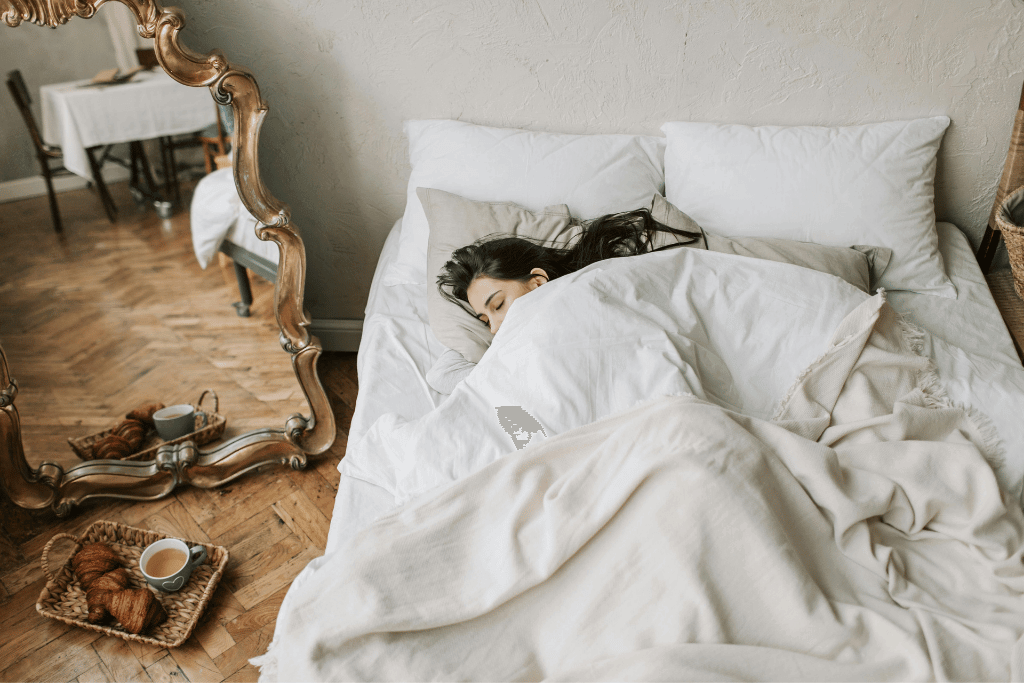 白い寝具に包まれてベッドで眠る女性と朝食