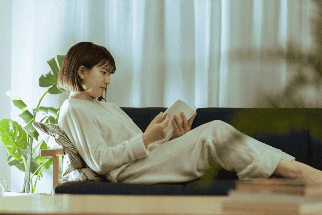 部屋でソファに寝そべりながら読書をする女性
